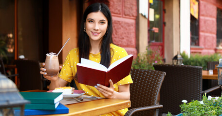 Poster - Beautiful young woman reading book in street cafe