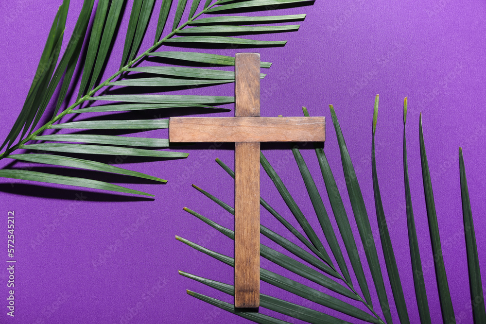 Wooden cross with palm leaves on purple background. Good Friday concept