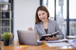 © David - Business Asian woman using calculator and writing make note with calculate doing math finance on an office desk. Woman working at office with laptop and tax, accounting, documents on desk.
