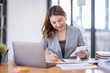 © David - Business Asian woman using calculator and writing make note with calculate doing math finance on an office desk. Woman working at office with laptop and tax, accounting, documents on desk.