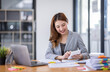 © David - Business Asian woman using calculator and writing make note with calculate doing math finance on an office desk. Woman working at office with laptop and tax, accounting, documents on desk.