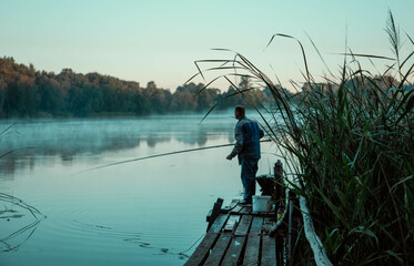  A man stands on a pier and fishes, dawn, summer.