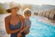 © Cavan Images - A mother wearing a hat holding her son in the pool during sunset