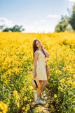 Fototapeta Kwiaty - girl walks in a yellow field of rapeseed. A woman with a bouquet of flowers in her bag