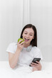 © itchaznong - Portrait of Good Healthy woman eating green apple and resting in bed at bedroom. Lifestyle at home concept.