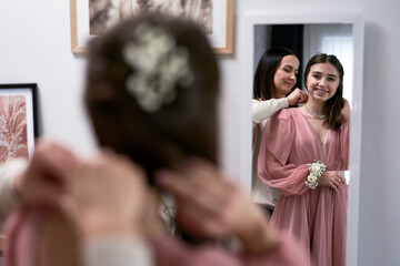 Caucasian mother helping daughter with wearing jewelry before prom