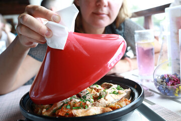 Woman lifting red lid of tagine