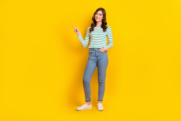 Full size photo of cute woman curly hairstyle striped shirt arm in pocket directing look empty space isolated on yellow color background