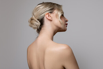 Young beautiful woman stands on her side with bare shoulders and back. Concept of hair and makeup, skin and body care