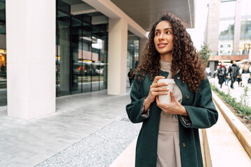 Young and cheerful woman walking with coffee cup through the city