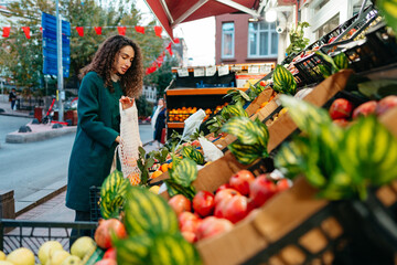 Young woman consumer choosing products to buy from local farmers market stand