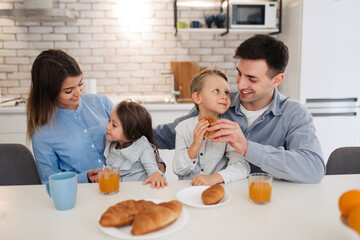 Family, eating and people concept - happy mother, father,daughter and son having breakfast at home on modern kitchen.