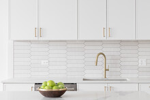 A Beautiful Kitchen Faucet Detail With White Cabinets, A Gold Faucet, White Marble Countertops, And A Brown Picket Ceramic Tile Backsplash.