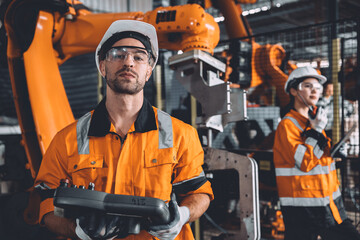 Engineer team service robot welding working in automation factory. People worker in safety suit work robotic arm software programming or replacing part in automated manufacturing industry technology.