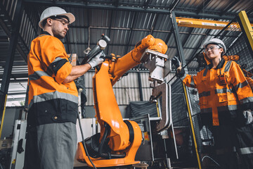 Wall Mural - Engineer team service robot welding working in automation factory. People worker in safety suit work robotic arm software programming or replacing part in automated manufacturing industry technology.