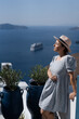 Tourist woman in blue dress with hat relaxing at sea view in the traditional village Thira. Walking Santorini tour, Greece, during her summer  crouise travel. European tourism attraction in Greece.