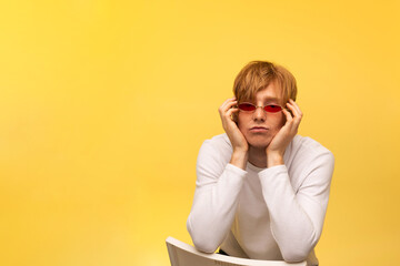Serious redhead european teenage boy with freckles and stylish pink glasses. model on a bright yellow background