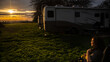 Young lady sitting in the sunlight of a sunset at campsite with Rv motorhome