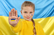Little girl with paint on hand and face near Ukrainian flag, focus on palm
