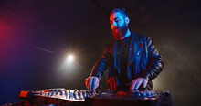 Cool Bearded Disc Jockey Working At Mixer Controller In A Nightclub. Authentic Dj Performing In Neon Lights And Smoke - Nightlife Concept 