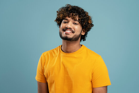 confident curly haired bearded indian man, wearing a bright yellow t-shirt, smiling a beautiful toot