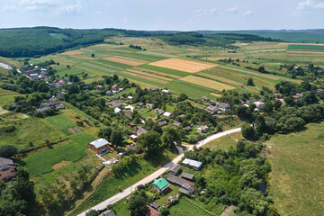 Wall Mural - Aerial landscape view of village houses and distant green cultivated agricultural fields with growing crops on bright summer day