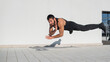 © Михаил Решетников - A man in black sportswear jumps while doing push-ups outdoors.