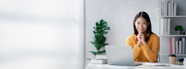 Wall Mural - Asian teenage woman sitting in white office with laptop, she is a student studying online with laptop at home, university student studying online, online web education concept.