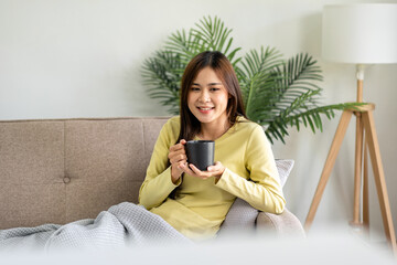 Wall Mural - Young asian woman is drinking coffee and lying on the big comfor