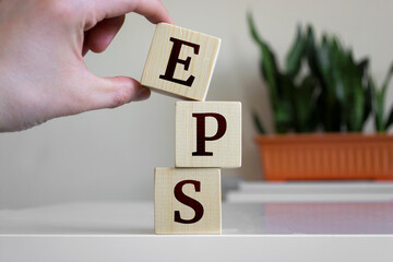 Wall Mural - Hand holding wood cube block with 'EPS' text. EPS - short for Earnings Per Share