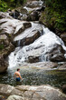 A young man swims in a pool at the base of a waterfall in Puerto Rico on an adventure on a sunny day.