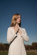 © Milou Dirks - portrait of young woman in white dress praying outside with blue sky