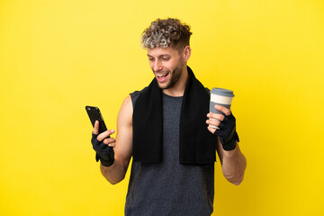 Wall Mural - Sport caucasian man isolated on yellow background holding coffee to take away and a mobile