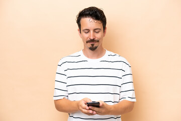 Wall Mural - Young caucasian man isolated on beige background sending a message with the mobile