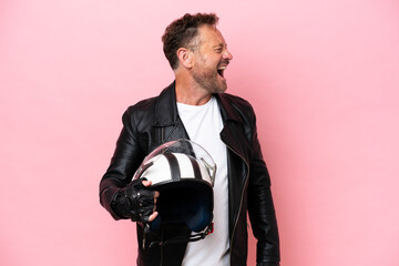 Middle age caucasian man with a motorcycle helmet isolated on pink background laughing in lateral position