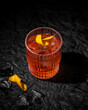 Negroni cocktail on black leather background. Italian IBA drink with gin, vermouth and orange. Fresh stir with ice. Classic alcoholic beverage at the bar in harsh light.  Luxury, rich taste. Close up