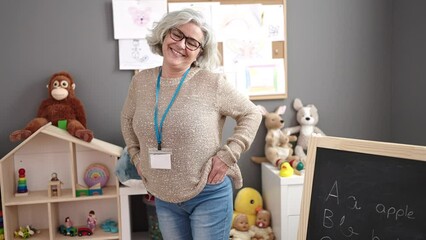 Poster - Middle age woman with grey hair preschool teacher smiling confident standing at kindergarten