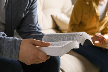 Couple sitting and reading holy Bible indoors, closeup