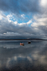 Wall Mural - view of boat on still tranquil sea with reflection of clouds and sky on water