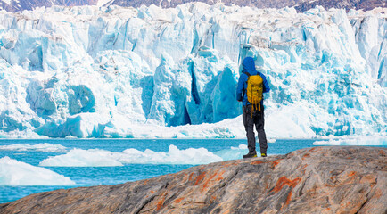 nvironmental Concept - A Man Hiker looking at melting glacier - Melting of a iceberg and pouring water into the sea - Greenland - Tiniteqilaaq, Sermilik Fjord, East Greenland