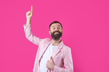 A man dressed in a pink jacket indicates the direction on a pink isolated background.