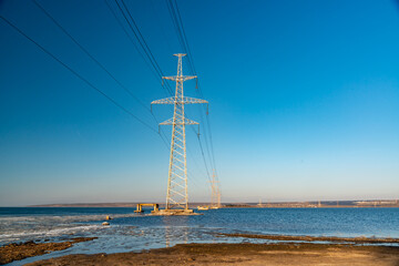 High-voltage power line against the background of the blue sky above the water of the lake