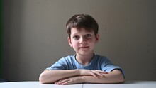 Portrait Of A 7-year-old Boy On A White Table. A Cute Child Looks At The Camera And Then To The Side. Calm Good Emotion