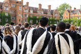 Fototapeta Londyn - back view of Male and female fresh British Black African graduate students with gown and academic address walk in campus of  University, UK during congregation day.
