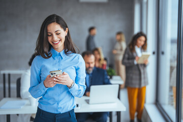 Wall Mural - Young businesswoman in the office and texting on smartphone. Beautiful businesswoman using mobile phone in modern office. Businesswoman with smartphone sitting near the window and having fun 