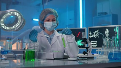 Wall Mural - A female scientist using a glass pipette picks up a green liquid and drops it onto a sample in a petri dish. The woman examines it and writes down the data of the study. Biotechnological laboratory.