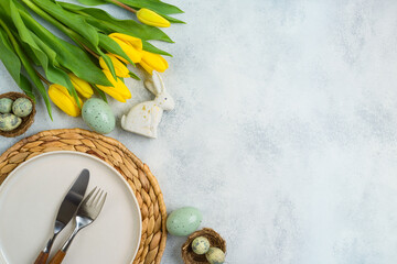 Wall Mural - Easter festive table setting with easter eggs decoration and yellow tulips flowers on bright background. Top view, flat lay