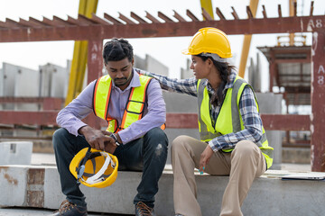 Asian Indian man worker feeling sad and upset while sitting at construction site. Female worker colleague supporting and consolation him.