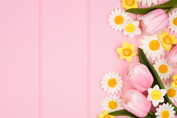 Wall Mural - Side border of springtime flower decorations. Above down view over a pastel pink wood background. Copy space.
