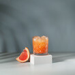 Fruity summer cocktail with red grapefruit and ice. Minimal cold drink layout. Grapefruit juice on color background. 